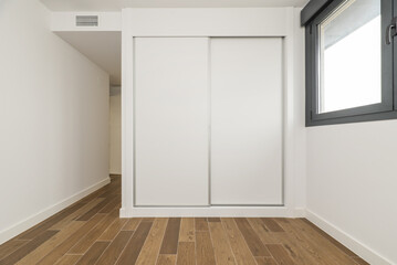 Empty room with a built-in wardrobe with white wooden sliding doors, black anodized aluminum...