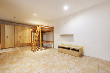 Large room with stoneware floors, wooden structure for a raised double bed and cabinets covering...