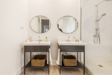 Designer cloakroom with vintage white porcelain twin sinks on metal cabinets and old round mirrors