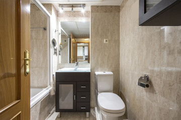 Small bathroom with dark wood cabinet with drawers, frameless mirror on the wall, marble tile and flooring and white shower stall