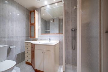 Small bathroom with dark wood cabinet with drawers, frameless mirror on the wall, marble tile and flooring and white shower stall