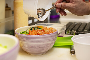 A chef preparing a salmon poke bowl with poppy seeds in an Asian kitchen