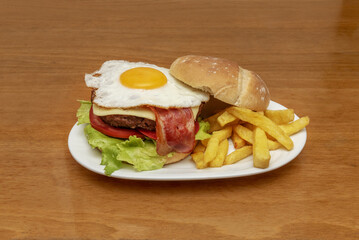 A delicious beef burger with bacon, cheese slices, fried egg with yolk, fresh lettuce and tomato slices with a serving of home fries