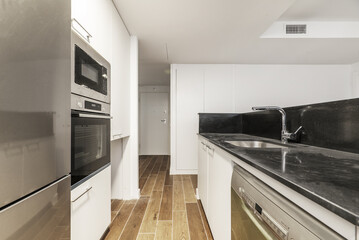 kitchen with an island with a black marble countertop, a column of stainless steel appliances and white wooden furniture