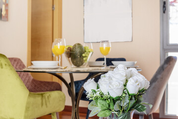 A bouquet of white artificial roses decorating a room with a table full of fruit and glasses of orange juice