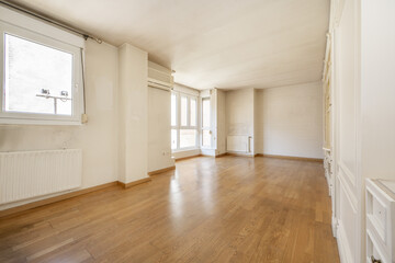 Empty living room with white lacquered wooden bookcase, large windows and white aluminum windows and oak parquet floors