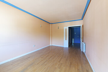 Empty living room with light peach painted walls and ceiling, blue plaster cornices and wooden flooring