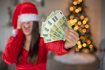 Frau mit Weihnachtsmütze und Geld als Geschenk in der Hand. Bokeh von den Lichtern eines...