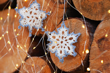 crocheted snowflakes decorations for the Christmas tree on the background of slices of large trees and bright led lanterns