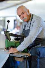 senior man using industrial machine to put eyelets in material