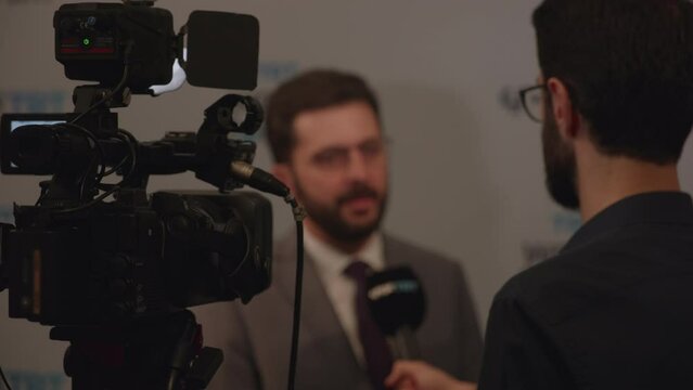 The reporter asks the man being interviewed a question, hands him a microphone, and the television camera is recording.