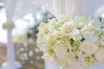 white rose arch decorated with orchid flowers In a beautiful seaside wedding ceremony surrounded by white cloth There is a beautiful bokeh in the background.