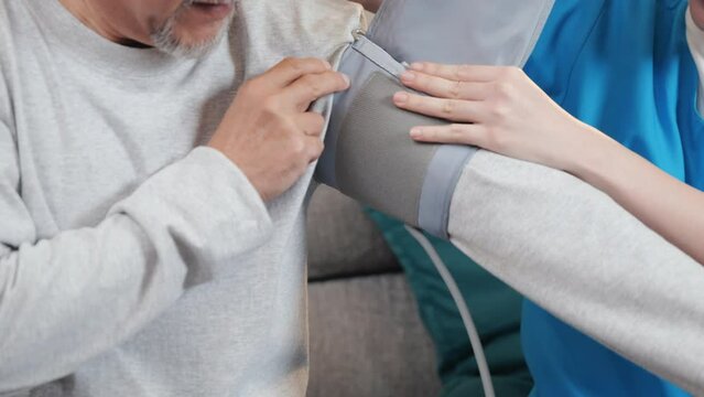 Asian doctor woman examine do checking old man client heart rate with pulsimeter monitor, nurse visit patient senior man at home she measuring arterial blood pressure on arm in living room, Healthcare