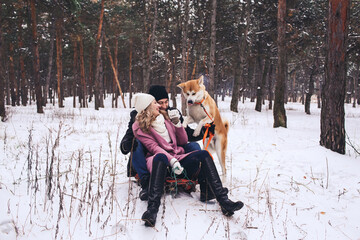 Fototapeta na wymiar A couple and a dog are sledding in a winter forest. Fun walk with the dog in winter