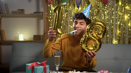 Young man with golden balloon 18 celebrating eighteen birthday at home.