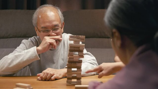 Smiling parent having fun play build constructor tower of wooden blocks, Happy grandparents Asian family enjoy playing toy block with little daughter together in home living room at night time