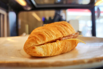 A piece of baked croissant ham cheese which is served in white dish. Bakery snack food object photo, close-up and selective focus.
