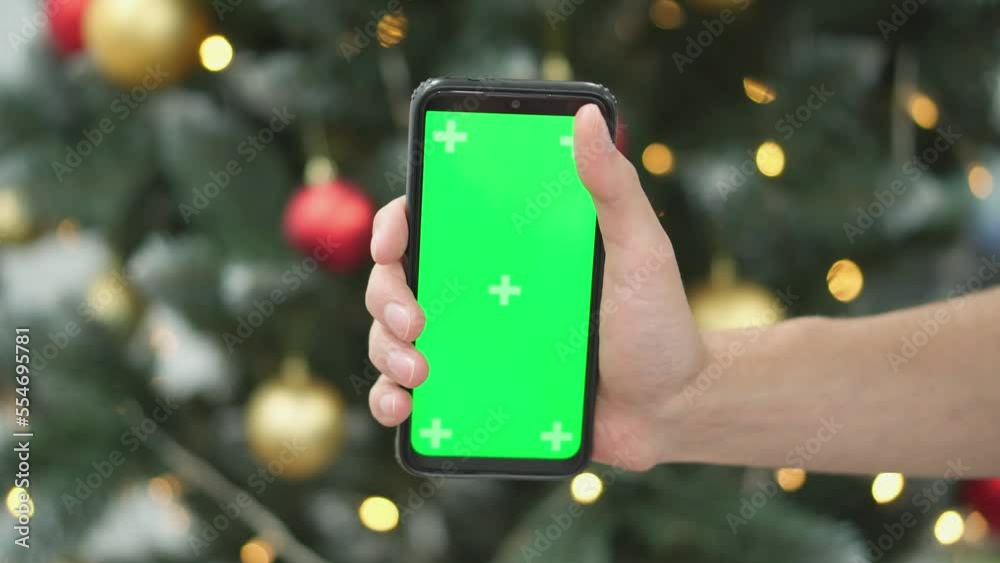 Poster human is holding a smartphone with a green screen on the background of christmas tree branches with 