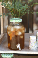 Tea dispenser stand with fresh orange tea outdoors with paper cups.
