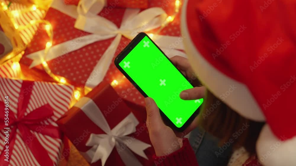 Poster human is holding a smartphone with a green screen on the background of christmas tree branches with 