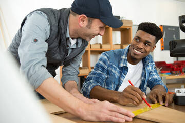 carpenter guiding apprentice working in workshop