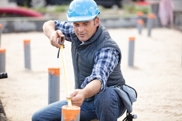 construction worker checking sanitation pipes with measuring tape