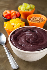 Açaí on a bowl with strawberry, mango and grape on colorful bowls over a stone background