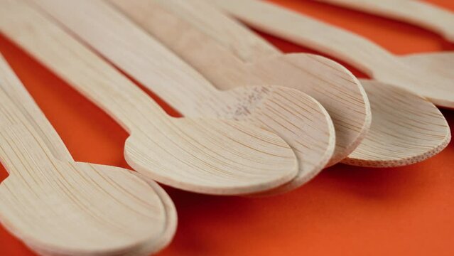 Wooden bamboo disposable spoons on a bright colored orange background. Ecological eco recycled kitchen utensils