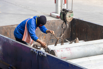 A worker attaches chains from a crane to concrete tubes on the load space of a truck