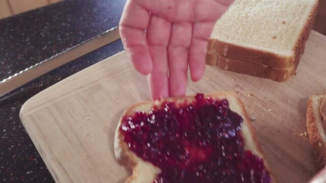 Preparing peanut butter and jelly sandwich on a wood cutting board.
