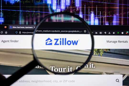 Zillow company logo on a website with blurry stock market developments in the background, seen on a computer screen through a magnifying glass