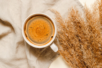 Cup of coffee on beige linen towel with dry pampas grass, aesthetic minimal composition, top view
