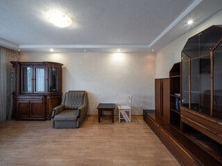 Modern interior of living room in apartment. Wooden cupboard, table and chair. Grey armchair.