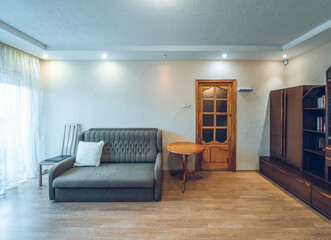 Modern interior of living room in apartment. Wooden furniture. Grey sofa. Door to balcony.