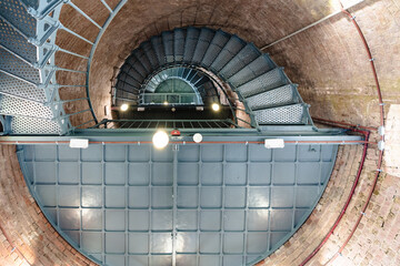 Image looking up toward ceiling of a green spiral, circular metal, iron staircase with red brick walls in a lighthouse.