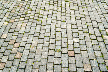 The texture of the stone pavement with grass between the stones close-up.