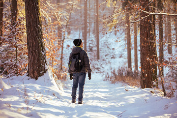 turysta z plecakiem wędrujący po zaśnieżonym lesie zimą  - obrazy, fototapety, plakaty