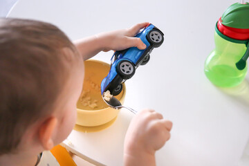 happy child eats at the table on his own. Healthy food, the child feeds the machine. Playing and feeding the baby. Ways to feed your baby