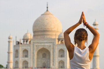 Girl doing yoga in front of the Taj Mahal. Tree pose. - obrazy, fototapety, plakaty