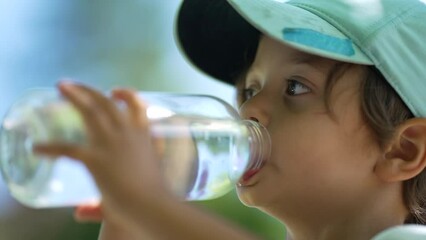 Young boy drinking water from bottle during hot sunny day. Male kid quenching thirst. Child hydrating himself in slow motion