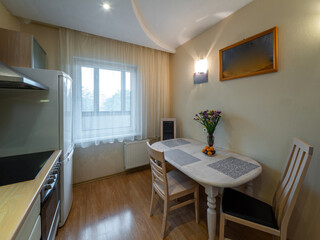 Modern interior of kitchen in apartment. Table and chairs. Fridge, oven and fan. Window with tulle.