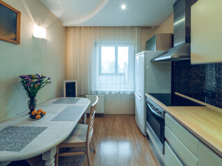 Modern interior of kitchen in apartment. Table and chairs. Fridge, oven and fan. Window with tulle.