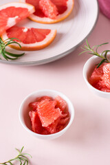 Juicy grapefruit slices and rosemary in a bowl on the table. Cocktail ingredients. Vertical view