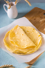Stack of flat mexican corn tortillas on wooden board on table. Vertical view