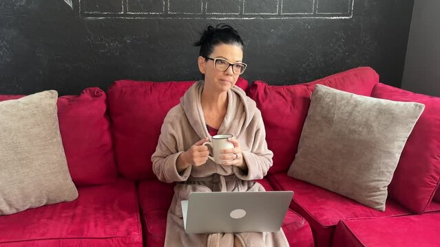 beautiful caucasian woman smiling and talking on video chat or online therapy session with glasses while holding a mug and drinking 4k natural light