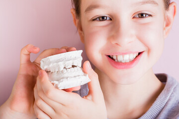 A girl with crooked teeth holds a plaster cast of her teeth. Dentistry and orthodontics