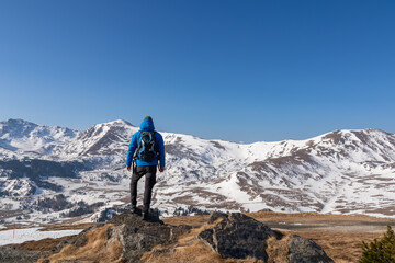 Fototapeta premium Rear view of man with backpack looking at snow capped mountain peak Zirbitzkogel and Kreiskogel in Seetal Alps, Styria (Steiermark), Austria, Europe. Hiking trail Central Alps in winter on sunny day