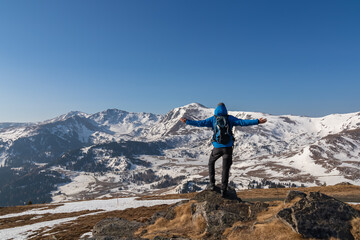 Obraz premium Rear view of man spreading arms with backpack looking at snow capped mountain peak Zirbitzkogel and Kreiskogel in Seetal Alps, Styria (Steiermark), Austria, Europe. Hiking trail in spring on sunny day