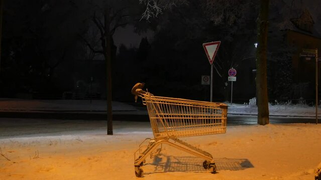 An empty cart from a supermarket on the street on a dark winter evening in the light of lanterns