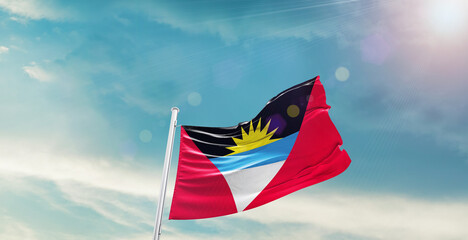 waving flag of Antigua and Barbuda in blue sky. the symbol of the state on wavy cotton fabric.